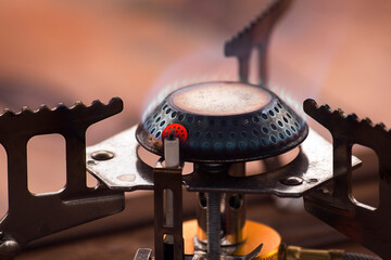 A close-up of a portable camping gas stove burning with blue fire. A piezo ignition is installed on the burner.