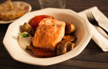 steamed salmon fillet on a pillow of fried mushrooms and tomatoes in a white bowl