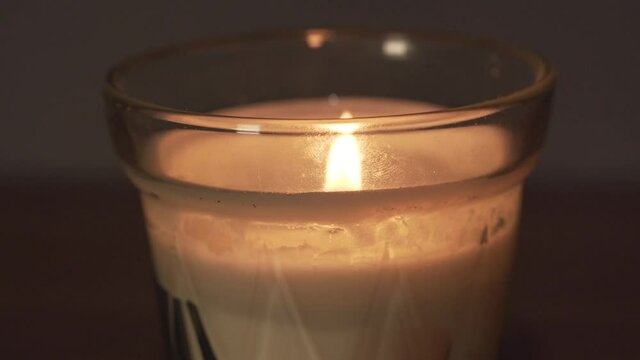 Close macro view of glass white wax candle and bright yellow flame at home. Decoration object