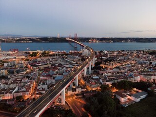 Aerial view of April 25th bridge with Christ the King statue (Cristo Rei) in background at sunset, view of Lisbon skyline at night, Alcântara, Lisbon, Portugal.