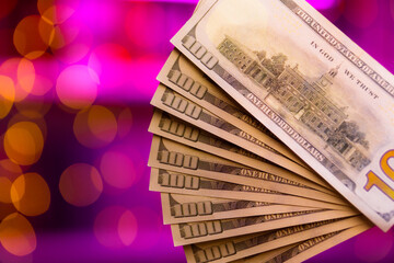 Lots hundred dollar bills on a purple background with a beautiful bokeh. The theme of cash settlement in a brothel or casino. USD money in macro photography in pink lighting.