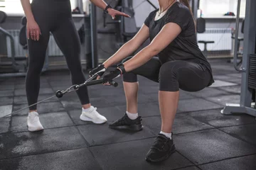Tuinposter Cropped shot of a woman doing glutes exercise at the gym with personal trainer © mad_production