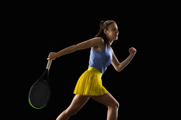 Young caucasian woman playing tennis isolated on black studio background in action and motion, sport concept