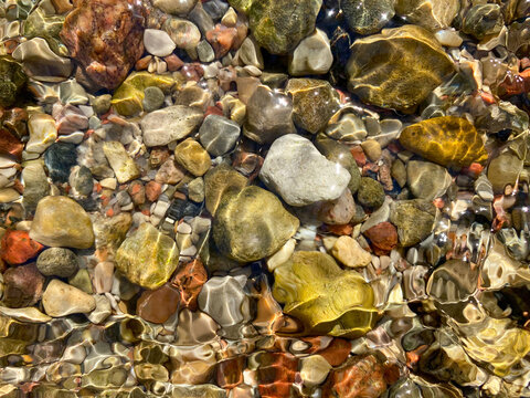 Background of colored river stones or pebbles under water. Top view. Clean and clear water