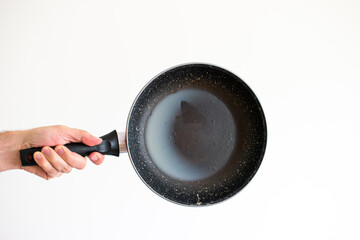 Caucasian male hand holding an old frying pan stained with hardened white lard grease and burned...