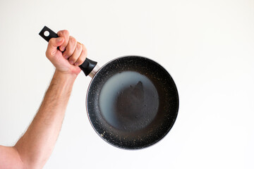 Caucasian male hand holding an old frying pan stained with hardened white lard grease and burned oil isolated on white.