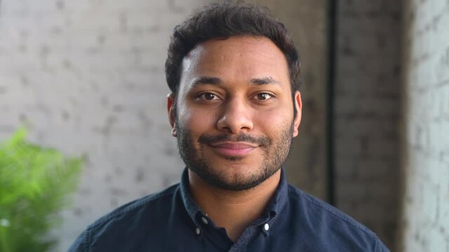 Confident hindu male entrepreneur looks at the camera and smiles, handsome mixed-race businessman in smart casual shirt laughs friendly standing indoor, headshot