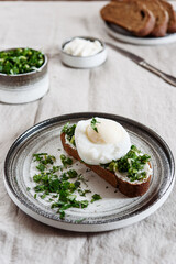 Healthy Breakfast with Poached Egg on toast with cream cheese and chopped mix of green onions, dill and parsley on greige linen tablecloth