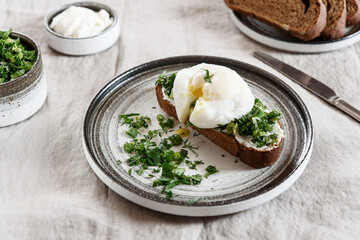 Healthy Breakfast with Poached Egg on toast with cream cheese and chopped mix of green onions, dill and parsley on greige linen tablecloth