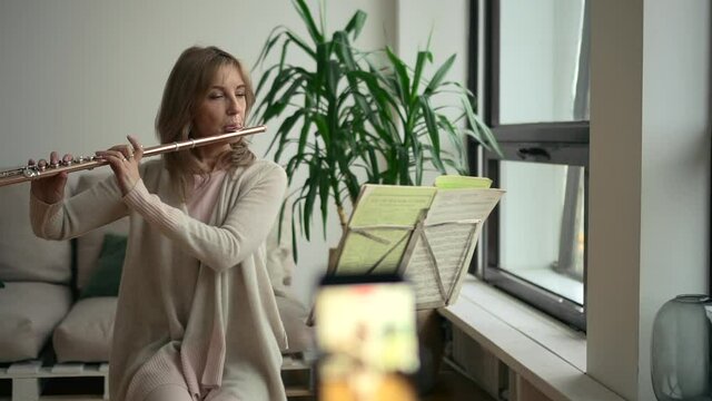 Middle aged woman playing flute and sitting in home room during self study.