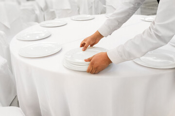 Close-up waiter man hands serving white banquet table at restaurant