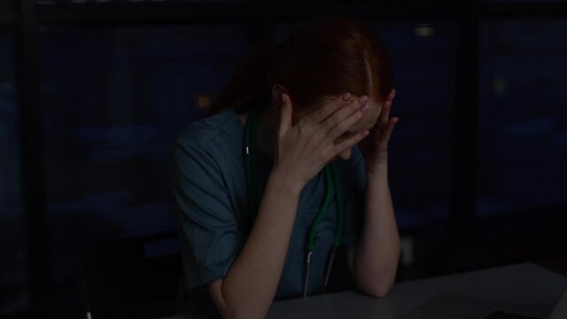 Close-up face of frustrated desperate young female doctor crying thinking about mistakes in dark hospital room near window at night. Exhausted woman physician depression after patient death.