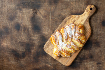 Sweet bun with cottage cheese and raisins on a serving board on a brown wooden table top view. The concept of homemade high-calorie pastries	