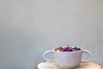 Ceramic bowl with fresh blueberries and strawberries and wooden tray on a table. Selective focus.
