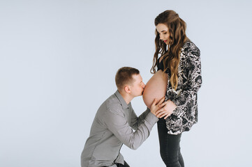 A loving man gently kisses the big belly of a pregnant woman on a white background cyclorama, photo studio. Photography, concept.