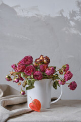 A bouquet of dry roses in a white teapot and one physalis on a table and a gray background. High quality photo