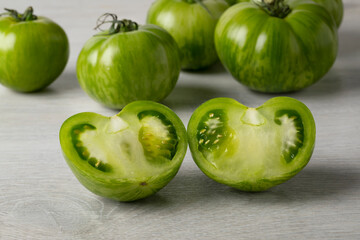 Whole and halved fresh green zebra tomato close up and tomatoes in the background 
