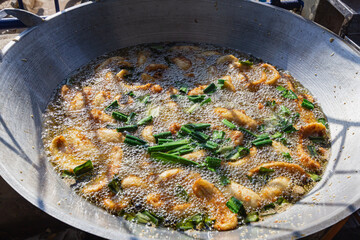 Bananas are fried in a large frying pan filled with oil.