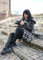 Adult caucasian woman sitting on the steps and watching at the watch. A woman checking what time it is. A person in rush and late. 
