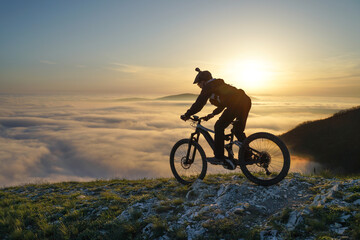 Fototapeta na wymiar Mountain Biker Riding Downhill Above the Clouds at Sunset.