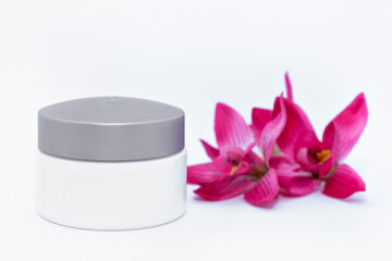 jar of face body cream moisturizer with pink tropical flower orchid frangipani on white background