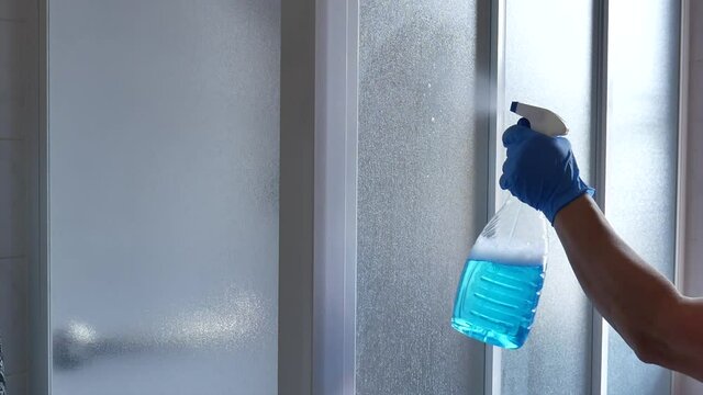 woman sanitizing shower box windows with blue bactericidal spray against viruses