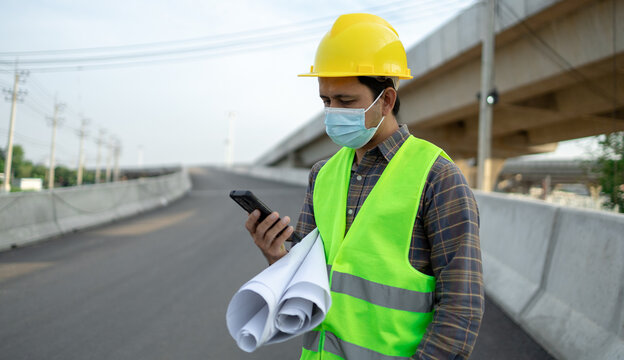 Construction worker protective face masks and use smartphone with blueprint paper at construction site background