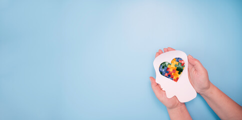 Female hands holding head with jigsaw puzzle heart shape. Autism spectrum disorder, autism awareness family support concept, World Autism Awareness Day