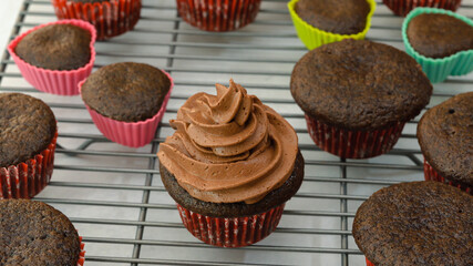 Frosting chocolate cupcakes with chocolate buttercream frosting, close up, woman hands, flat lay