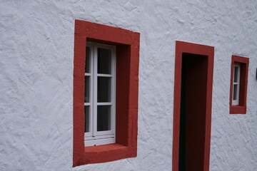 close up of a white house facade with white wooden windows and a red frame around the window and front door of a medieval house
