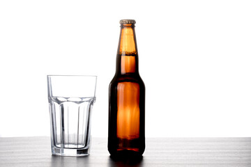 A brown beer bottle with no label with an empty glass on a table