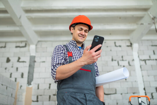 Engineer in red protective helmet with blueprint use smartphone at construction site