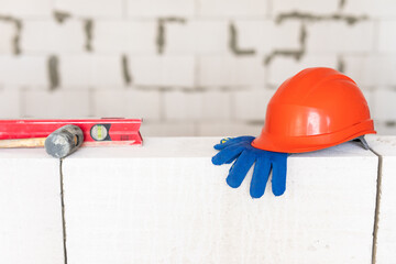Fototapeta premium Builder tools lays aerated concrete block at a construction site. Objects. Hemlet, gloves, water lavel, hammer on brick wall