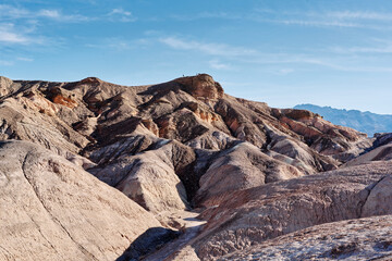 A family hike from Zabriskie Point in Death Valley national park in california. Huge sand dunes, terracotta mountains and hazy horizons are shining against clear blue sky in the midday sun.
