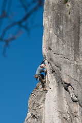 Male athlete climbs gray wall with blue sky in the background.