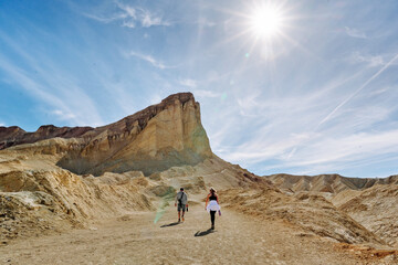 A family hike from Zabriskie Point in Death Valley national park in california. Huge sand dunes, terracotta mountains and hazy horizons are shining against clear blue sky in the midday sun. - obrazy, fototapety, plakaty
