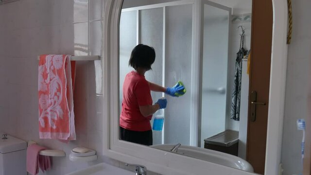 woman sanitizing shower box windows with blue bactericidal spray against viruses