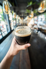 Close up pint of black beer on pub counter with hand man