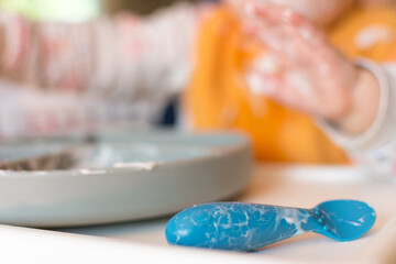 Silicone spoon and divided plate covered in yogurt sitting on a high chair tray; baby led weaning 