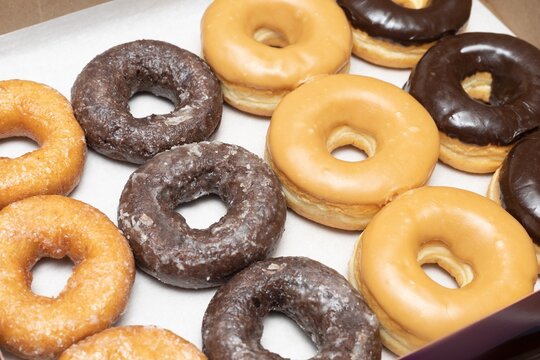 Top view picture of variety of assorted glazed donuts in a box. Unhealthy food concept 