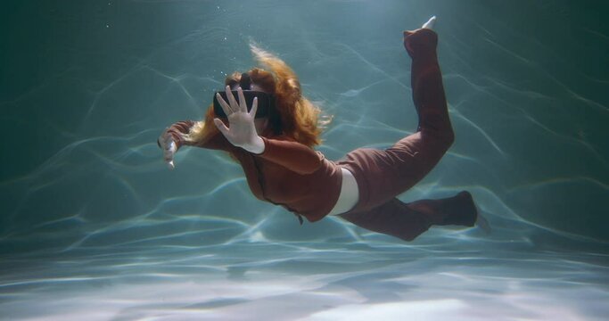 Beautiful young woman in virtual reality headset glasses floating under water touching invisible objects slow motion.