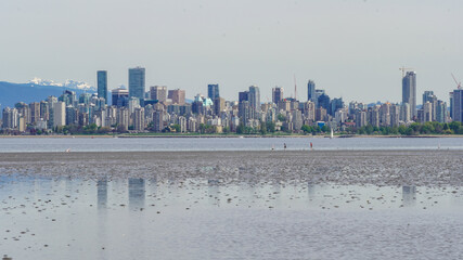 Panoramic view and shallow water reflection of Downtown Vancouver and snow mountain from low tide beach