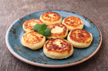 Cottage cheese pancakes or syrniki  on blue plate decorated with mint, closeup view. Russian, Ukrainian cuisine. Healthy tasty breakfast.