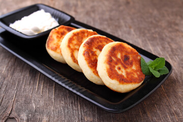 Cottage cheese pancakes or syrniki on black plate decorated with mint, closeup view. Russian, Ukrainian cuisine. Healthy tasty breakfast. Old wood background.