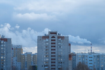 City landscape with houses and factory with a chimney and smoke in background. Winter evening in city. Production in a residential area, environmental and air pollution and danger to life and health.