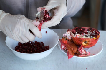 Woman in gloves is peeling a pomegranate over the plate on table, hands closeup. Woman is preparing...