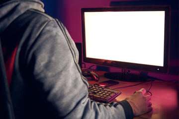An over the shoulder view of young adult man using computer in dark room at night with mouse and...