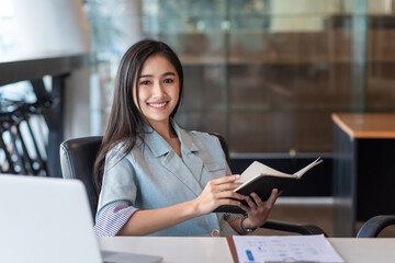 Fototapeta premium Young Asian businesswoman sitting holding document looking at the camera at the office.