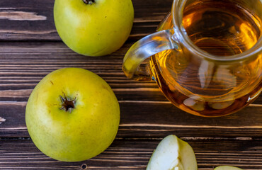 Green apples and jug with glass with apple juice on wooden background