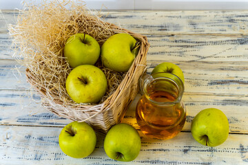 Green apples, basket with apples and jug with apple juice on wooden background